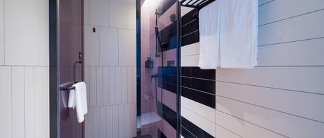 Un baño moderno con cabina de ducha de vidrio, pared con azulejos blanco y negro y un perchero con dos toallas blancas.