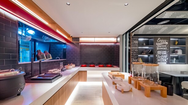 Una cucina moderna con un lungo bancone, pentole rosse e una lavagna con citazioni motivazionali.