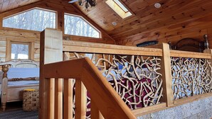 Ein Holzblockstube-Interieur mit Schlafkoje, Deckenventilator und dekorativer Holzgalerie.