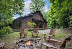 Une cabane rustique avec un foyer et des fauteuils Adirondack dans la cour.