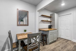 A compact kitchen with a wooden table, two chairs, a small potted plant, and white cabinetry.