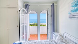 A bedroom with a bed, a white wardrobe, and a view of the sea through a glass door.