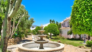A circular fountain with a tiered design, surrounded by a stone pathway and lush greenery.