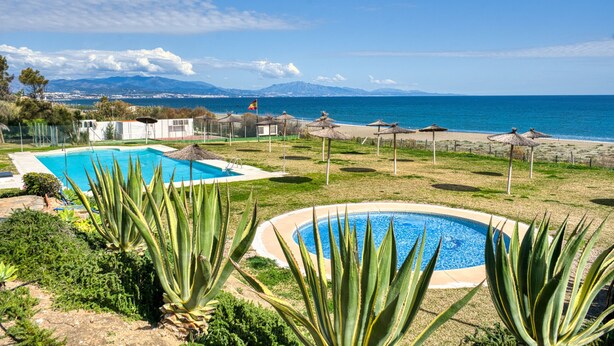 A pool area with two pools, a beach with umbrellas, and a view of the sea and mountains.