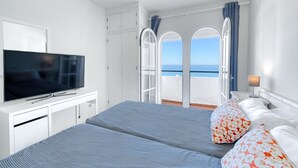 A hotel room with a bed, a TV, a desk, and a view of the sea.