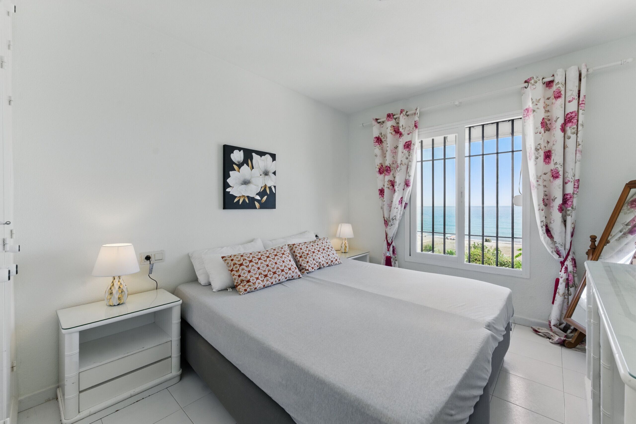 Une chambre à coucher avec un lit, des tables de chevet, une fenêtre avec des rideaux et un tableau au mur.