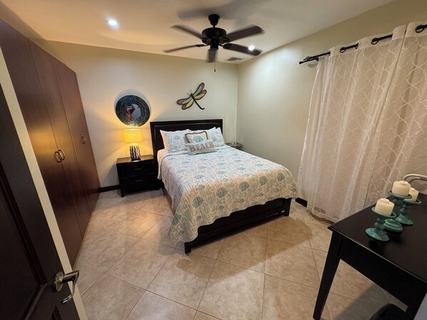 A bedroom with a bed, nightstand, ceiling fan, and a table with candles.