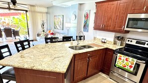Una cocina con encimeras de granito, armarios de madera, horno de acero inoxidable y comedor con mesa y sillas.