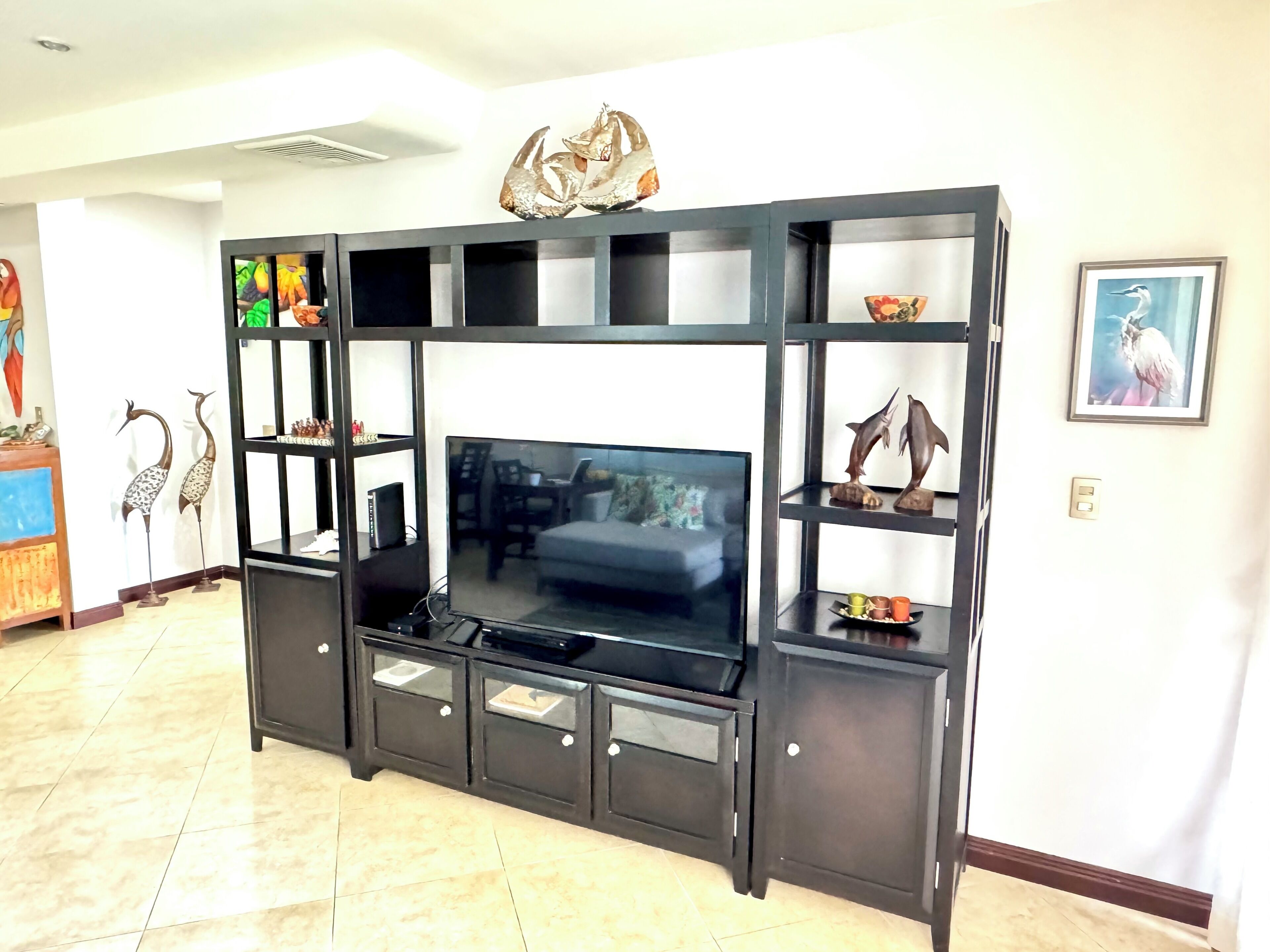 Un salon moderne doté d’un grand téléviseur à écran plat, d’un meuble de rangement noir avec des étagères et d’objets décoratifs.