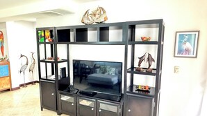Una sala de estar moderna con un televisor de pantalla plana grande, un mueble de entretenimiento negro con estantes y objetos decorativos.