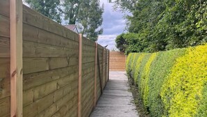 A narrow pathway flanked by a wooden fence and a neatly trimmed hedge.