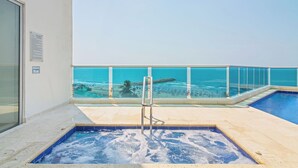 Una piscina en la azotea con barandilla de cristal con vistas a una playa.