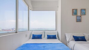 Habitación de hotel con dos camas, un ventanal grande con vista a la ciudad y tres cuadros en la pared.