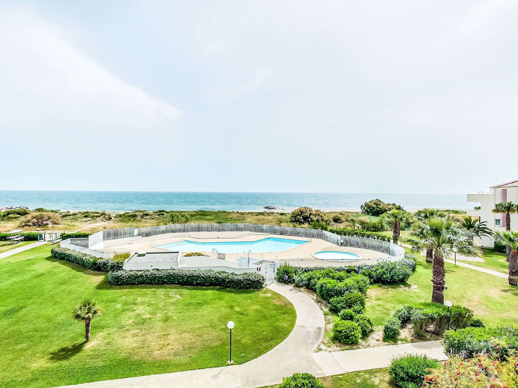 Zona de piscina con vista al mar, rodeada de vegetación y palmeras.
