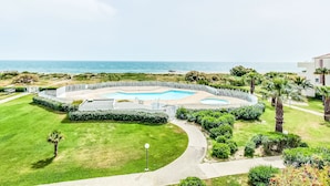 Zona de piscina con vista al mar, rodeada de vegetación y palmeras.