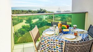Un balcón con una mesa dispuesta para dos, con vistas a un paisaje verde y el mar.