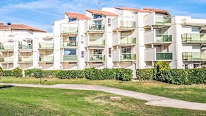Un moderno edificio residencial de varios pisos con balcones, cielo despejado y césped bien cuidado.