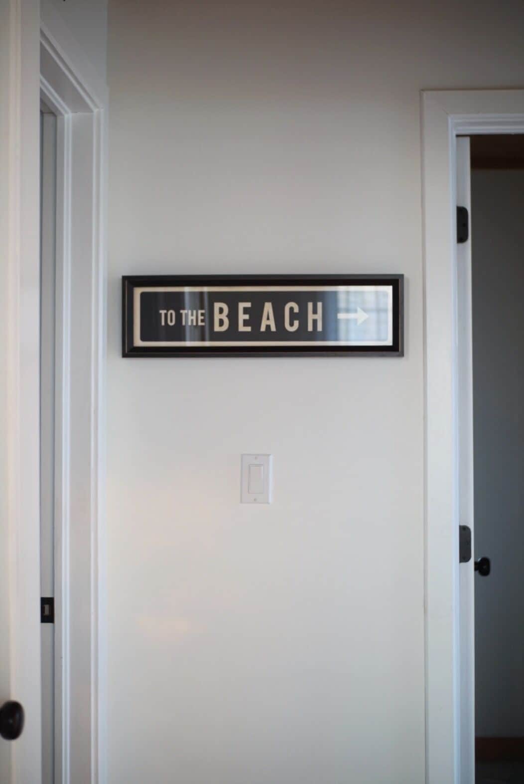 A framed sign on a wall that reads "TO THE BEACH" with an arrow pointing right.