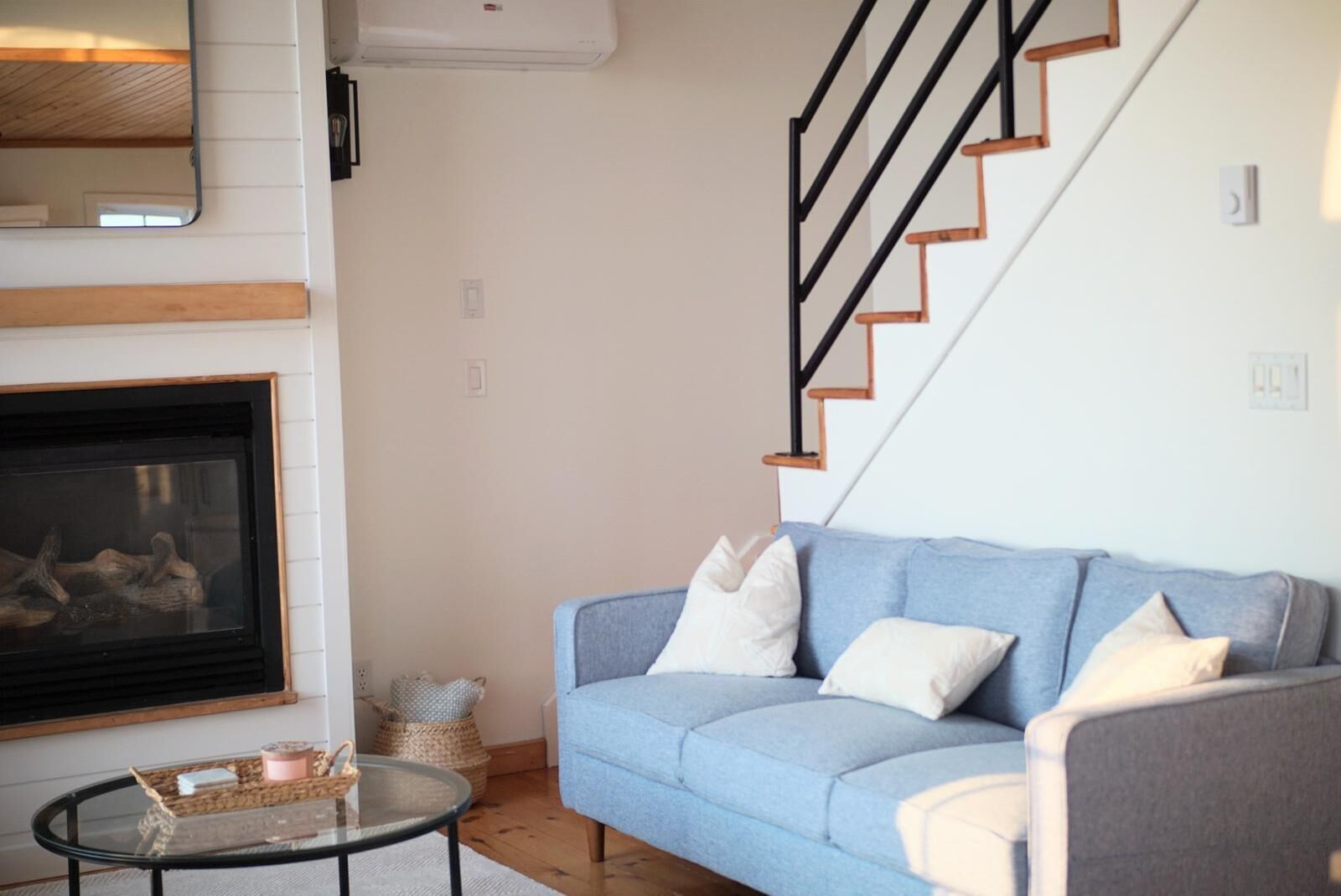 A living room with a blue sofa, a glass coffee table, a fireplace, and a staircase.
