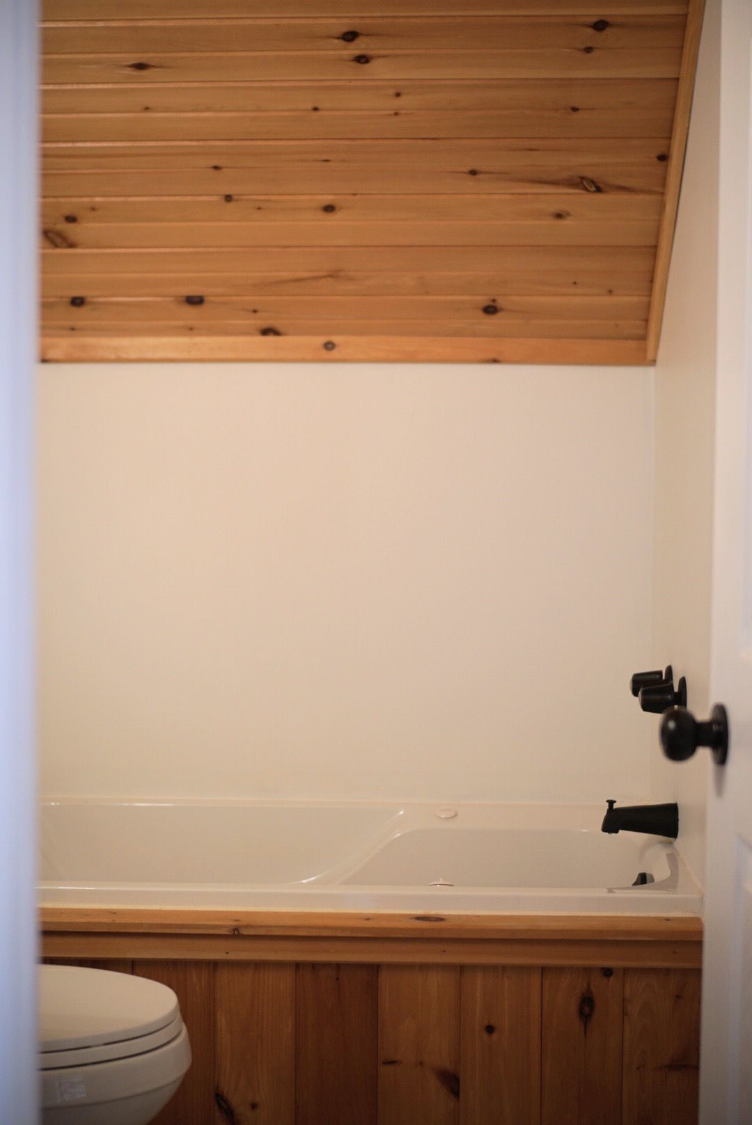 Un baño con techo de madera, una bañera blanca y un inodoro.