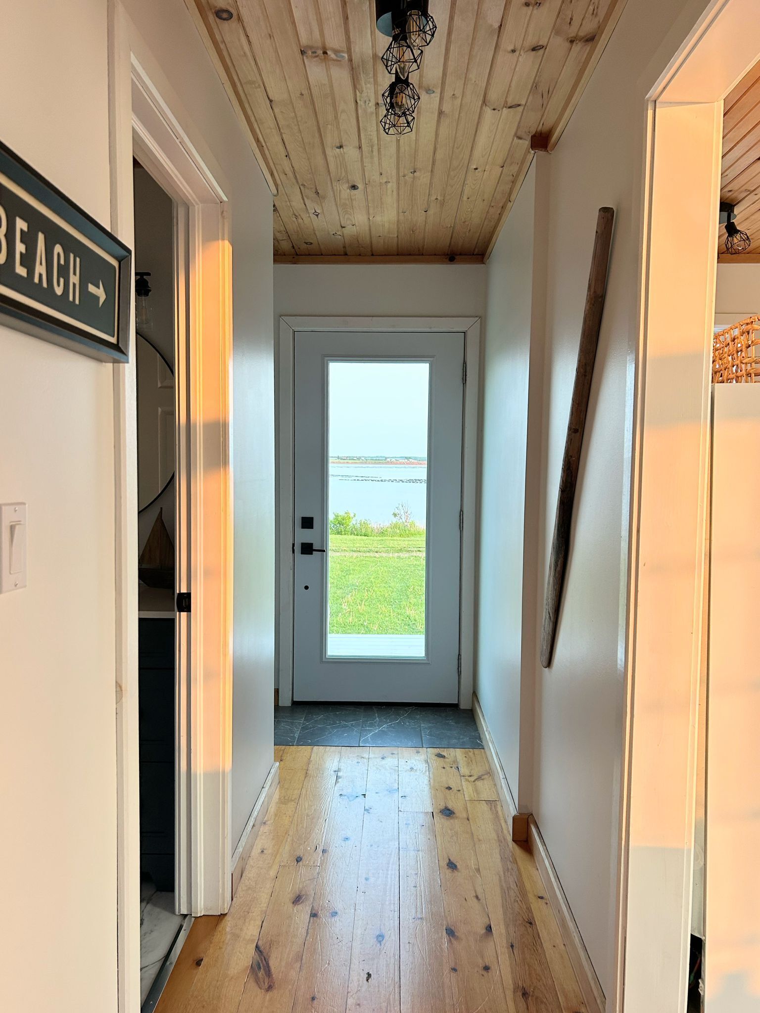 Un couloir avec un plancher en bois, une porte donnant sur l’extérieur et un panneau indiquant « Plage » sur la droite.