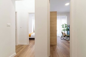 Un pasillo que conduce a un dormitorio con una cama, un panel de madera decorativo y un rincón de descanso con una silla y una planta.