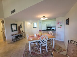 Un coin repas avec une table en bois et des chaises blanches, une cuisine avec des meubles blancs et un miroir décoratif au mur.