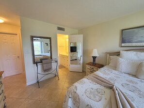Une chambre à coucher comprenant un lit, une table de chevet avec une lampe, une commode, un miroir et une porte donnant sur une autre pièce.