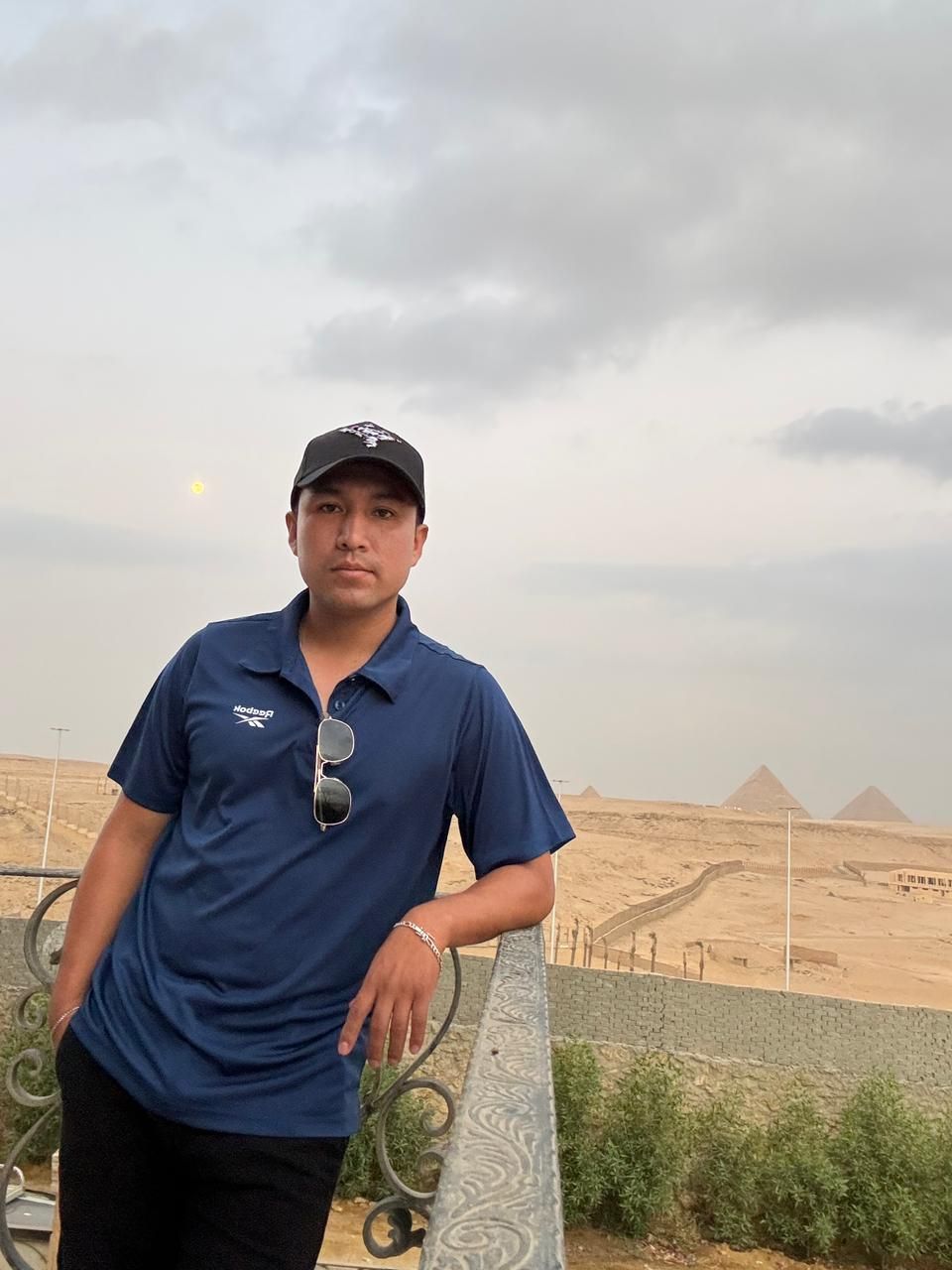 A person standing on a balcony overlooking a desert landscape with pyramids in the background.