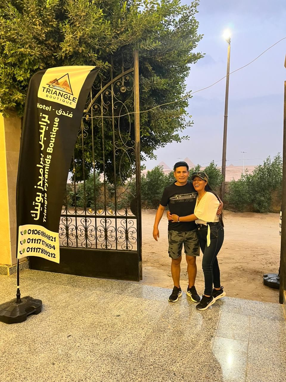 A man and a woman standing in front of a hotel entrance with a sign that reads 'TRIANGLE BOUTIQUE Hotel - de Paramus Boutique.'
