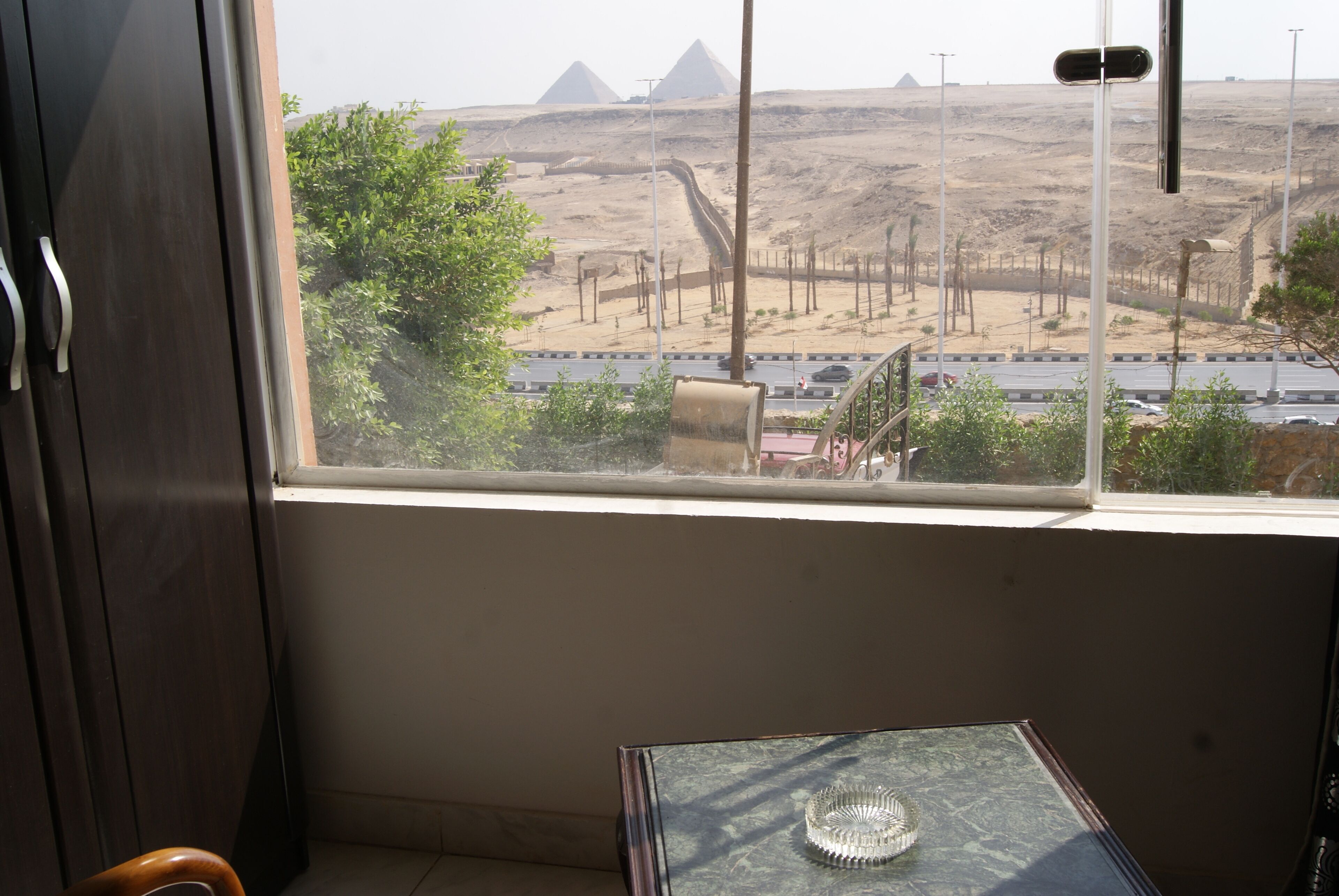 Ein Zimmer mit Fensterblick auf eine Wüstenlandschaft mit Pyramiden.
