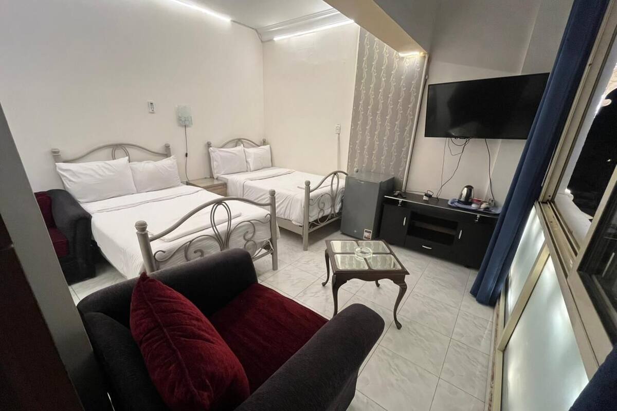 Habitación de hotel con dos camas, un sofá, una mesita, un televisor y un armario.