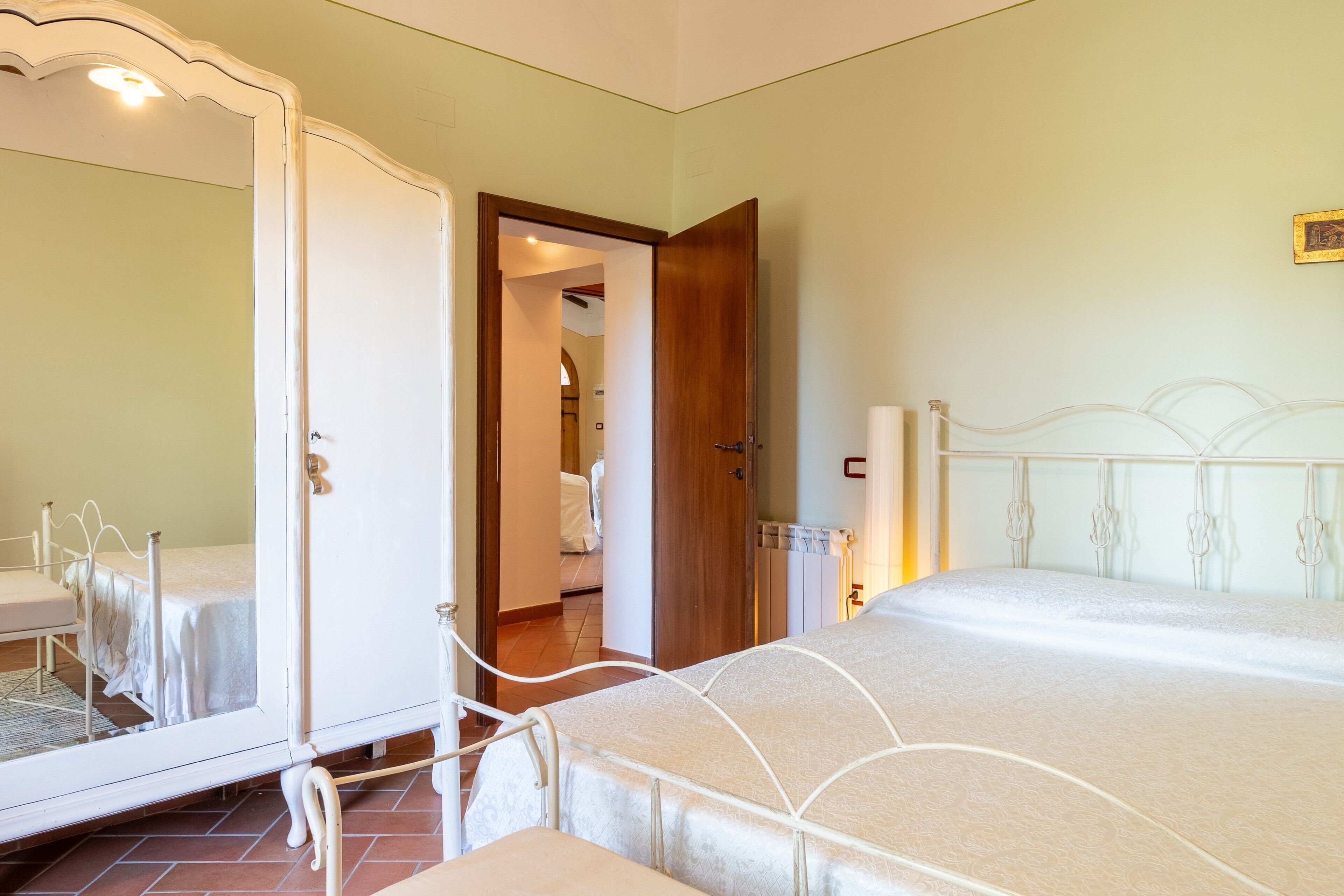 Un dormitorio con cama, armario, espejo y puerta que da a otra habitación.