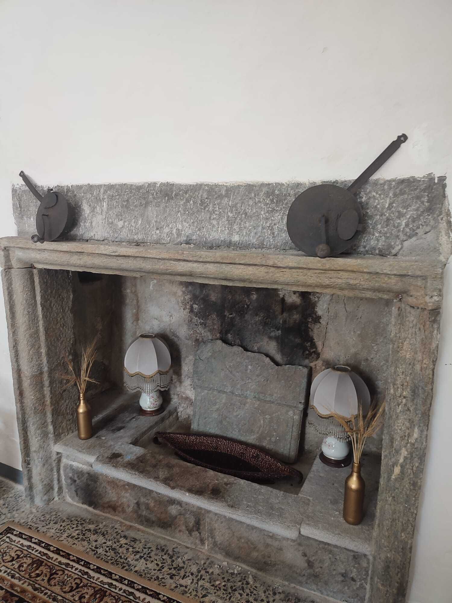 Une cheminée rustique avec un manteau en pierre, deux appliques murales et un vase décoratif contenant des roseaux.