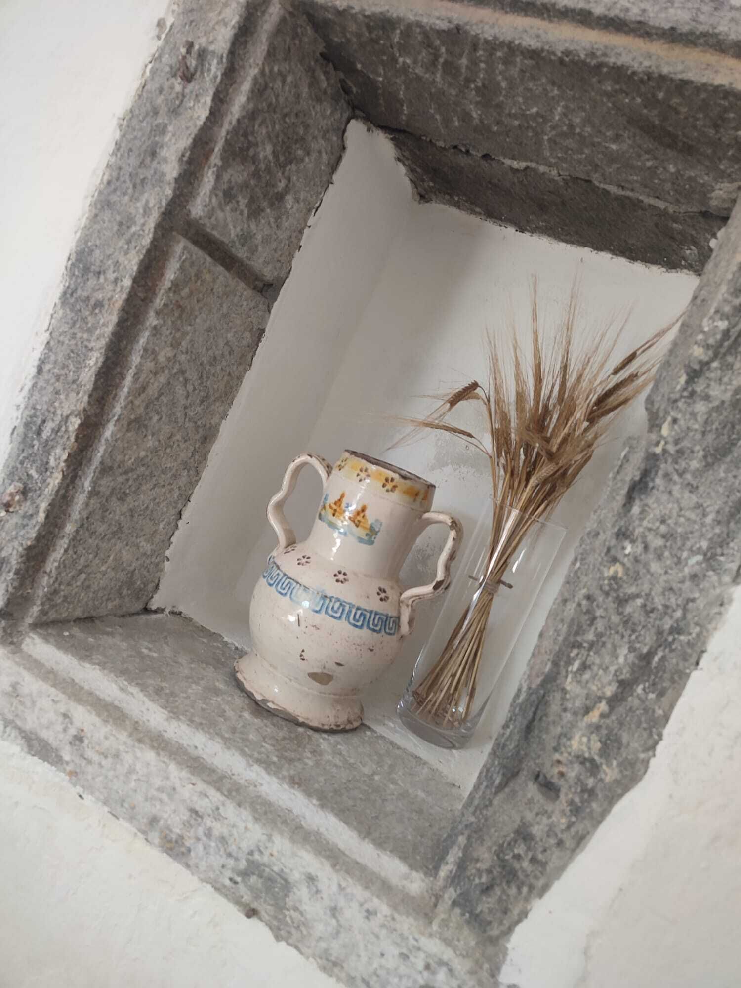 En lille stenindbygning med en keramikkanne og tørrede planter.