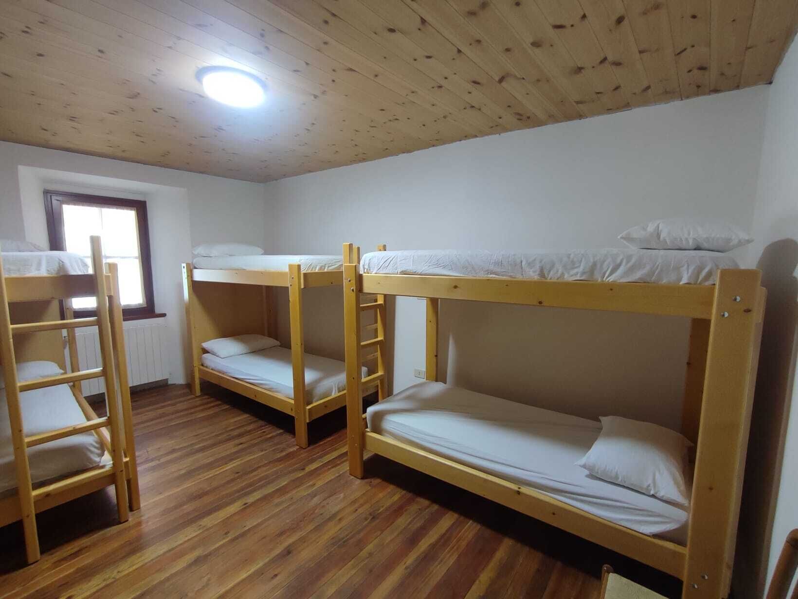 Ein Zimmer mit drei Etagenbetten, Holzböden, einem Fenster und einer Deckenleuchte.