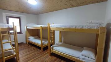 Ein Zimmer mit drei Etagenbetten, Holzböden, einem Fenster und einer Deckenleuchte.