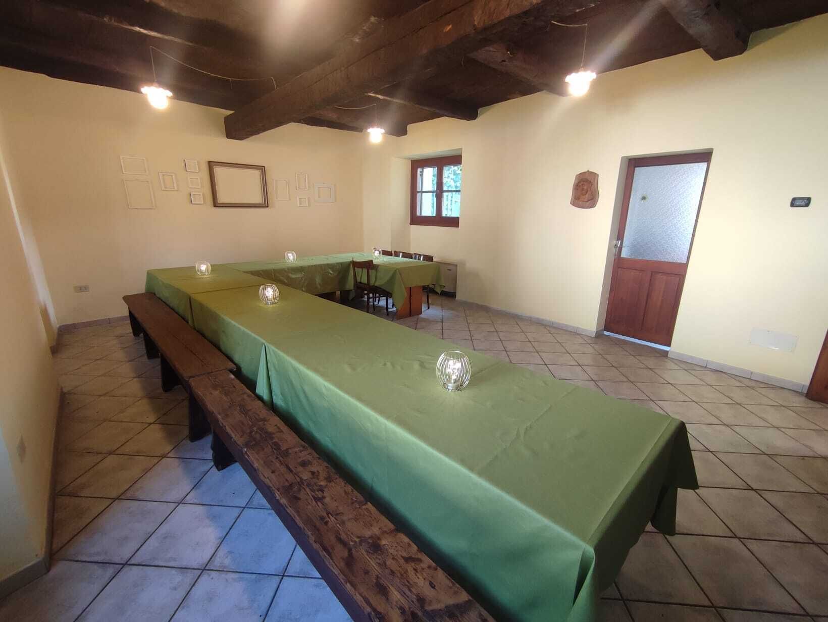 A dining area with a long table covered in green tablecloths, benches along the sides, and a wooden ceiling.