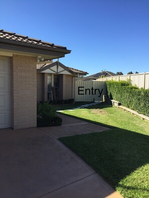A residential entryway with a clear pathway leading to a garage, a brick house, and a well-maintained lawn.