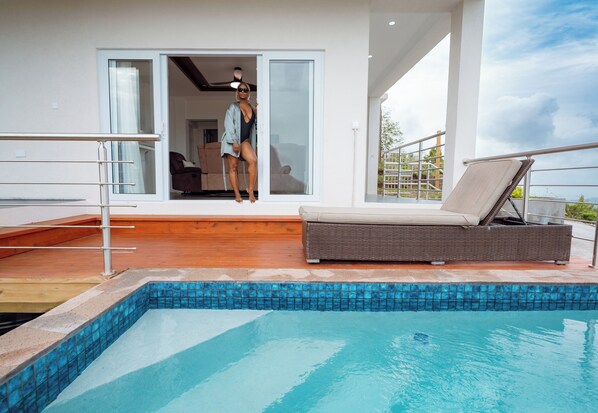 Un espace piscine extérieur moderne, offrant une vue dégagée sur la piscine, avec un fauteuil de relaxation en osier et une porte vitrée donnant accès à un espace intérieur.