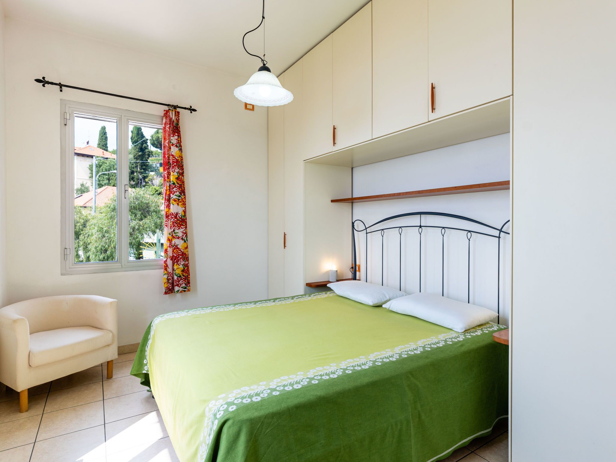 Une chambre à coucher avec un lit, une chaise, une fenêtre avec des rideaux et un luminaire suspendu.