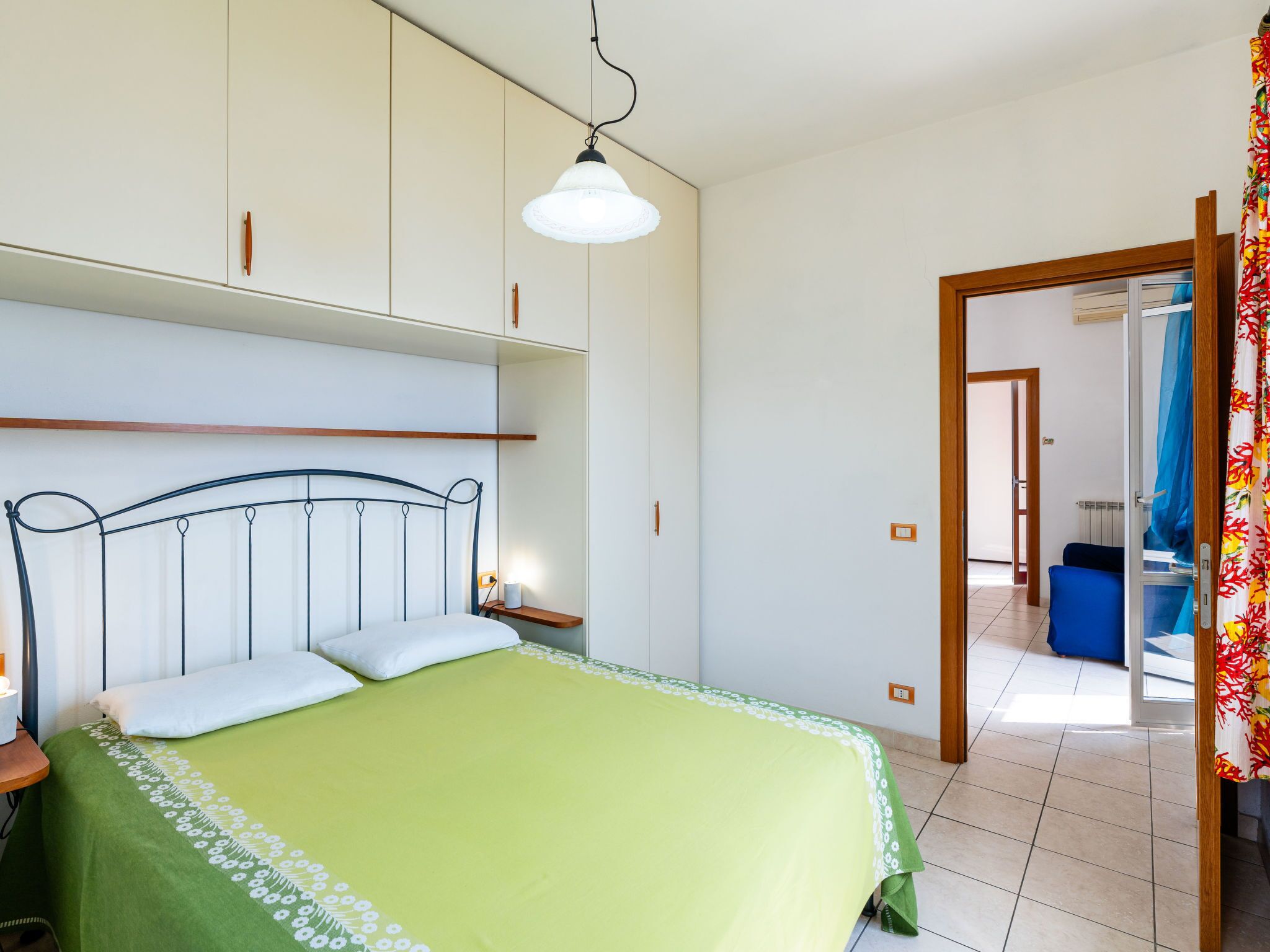 A bedroom with a bed, a bedside table, a hanging light, and a wardrobe.