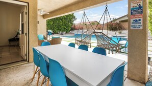 An outdoor patio with a pool, blue chairs, and a table. - Estrella Escape, Pool, Spa & Game Room Fun (Desert Hot Springs)