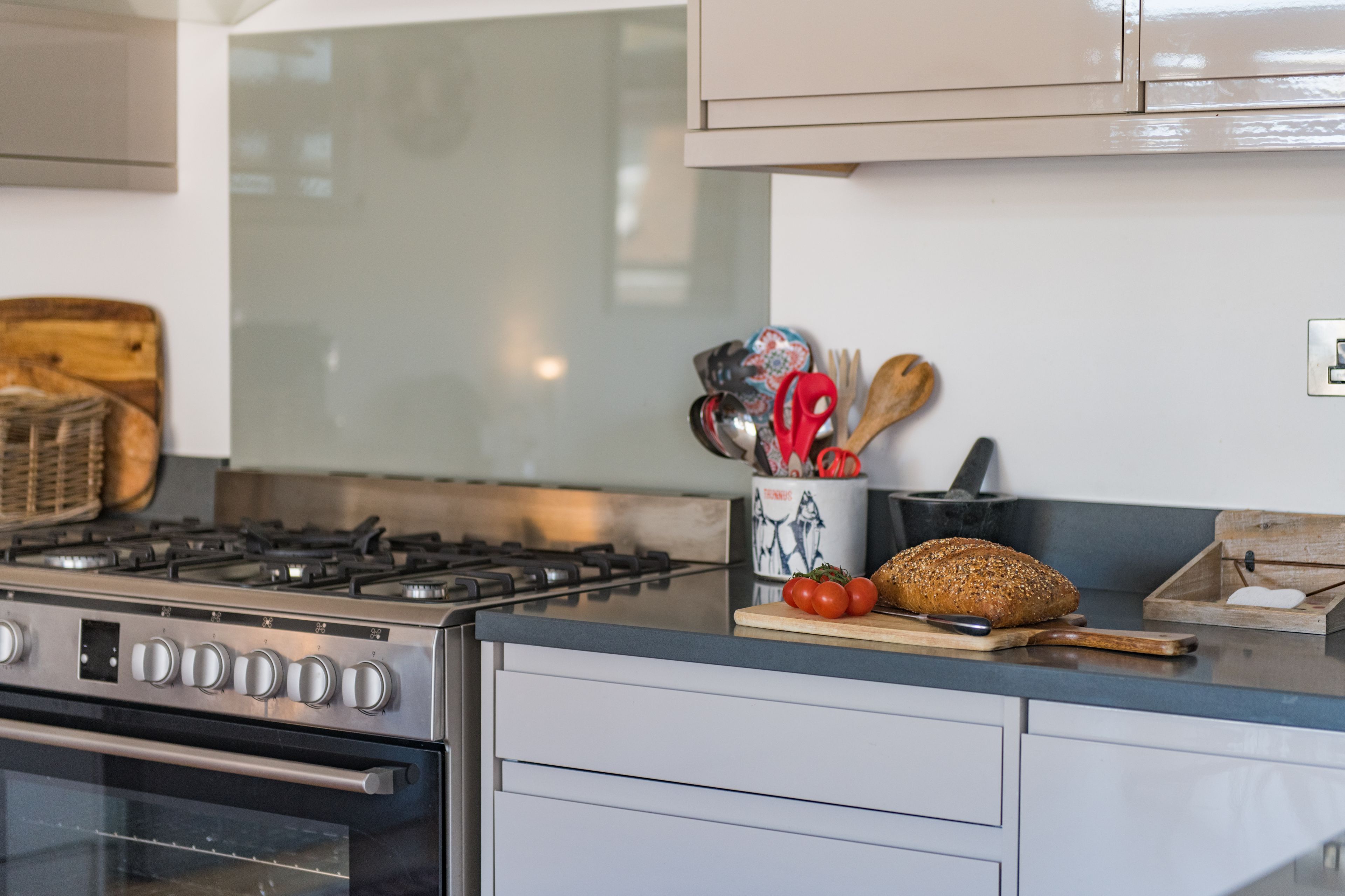 Una cocina con estufa a gas, horno y tabla de madera con pan y tomates.