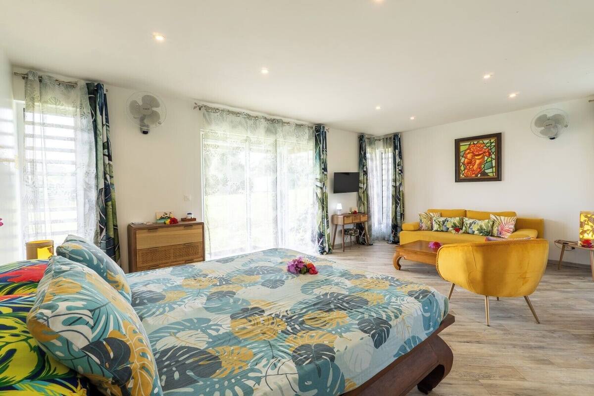 A bedroom with a bed, a yellow sofa, a desk, and a TV.