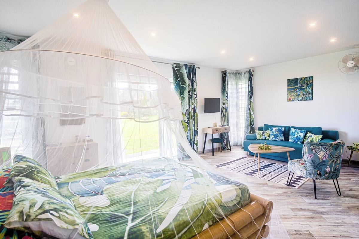 A bedroom with a canopy bed, a sitting area with a sofa and armchairs, and a view of the outdoors.