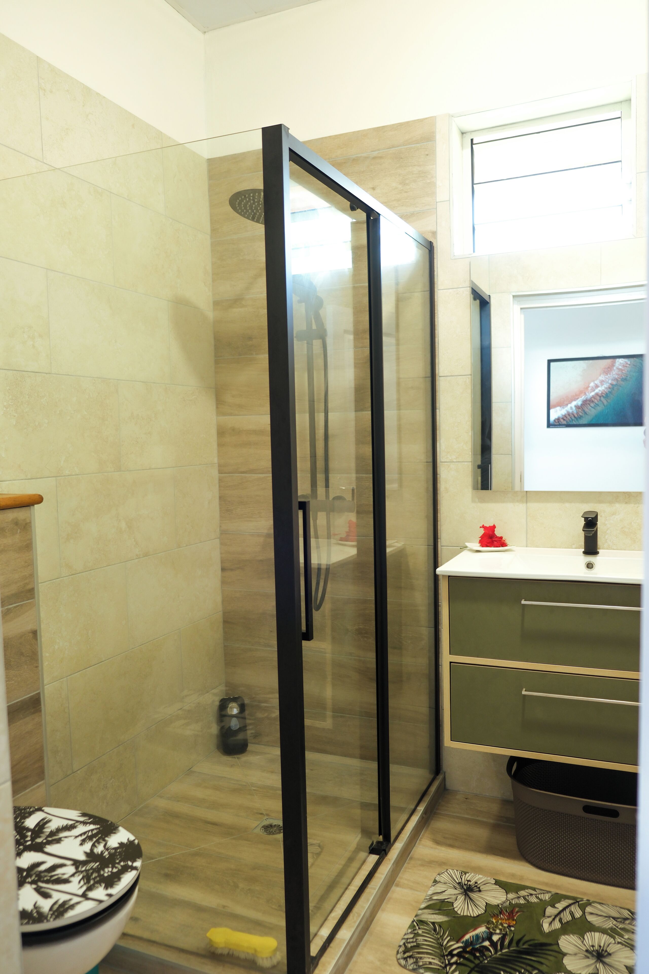 A bathroom with a glass-enclosed shower, a toilet with a leaf-patterned seat, and a sink with a green cabinet.