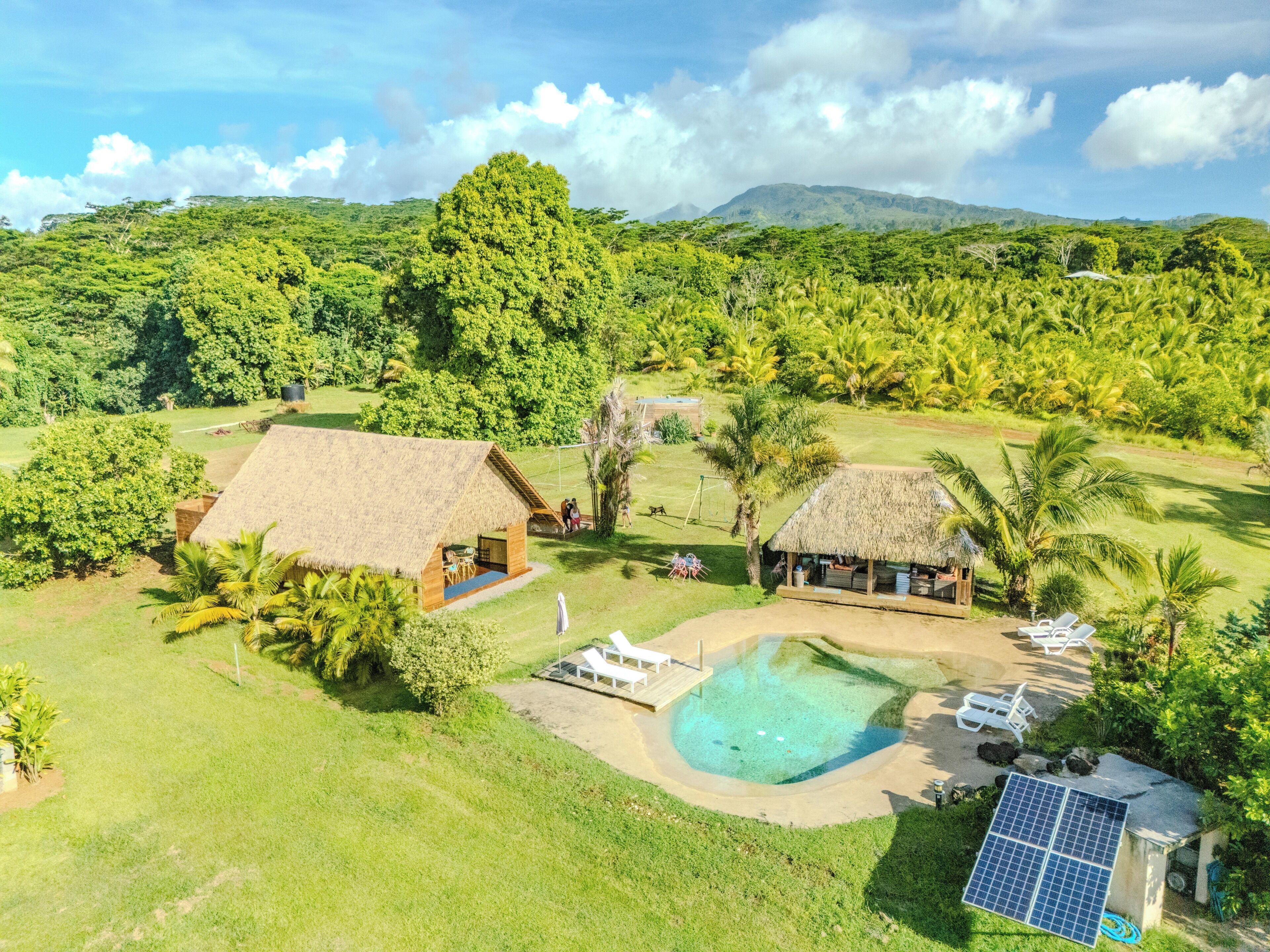 A resort with thatched-roof cabins, a swimming pool, and a solar panel.