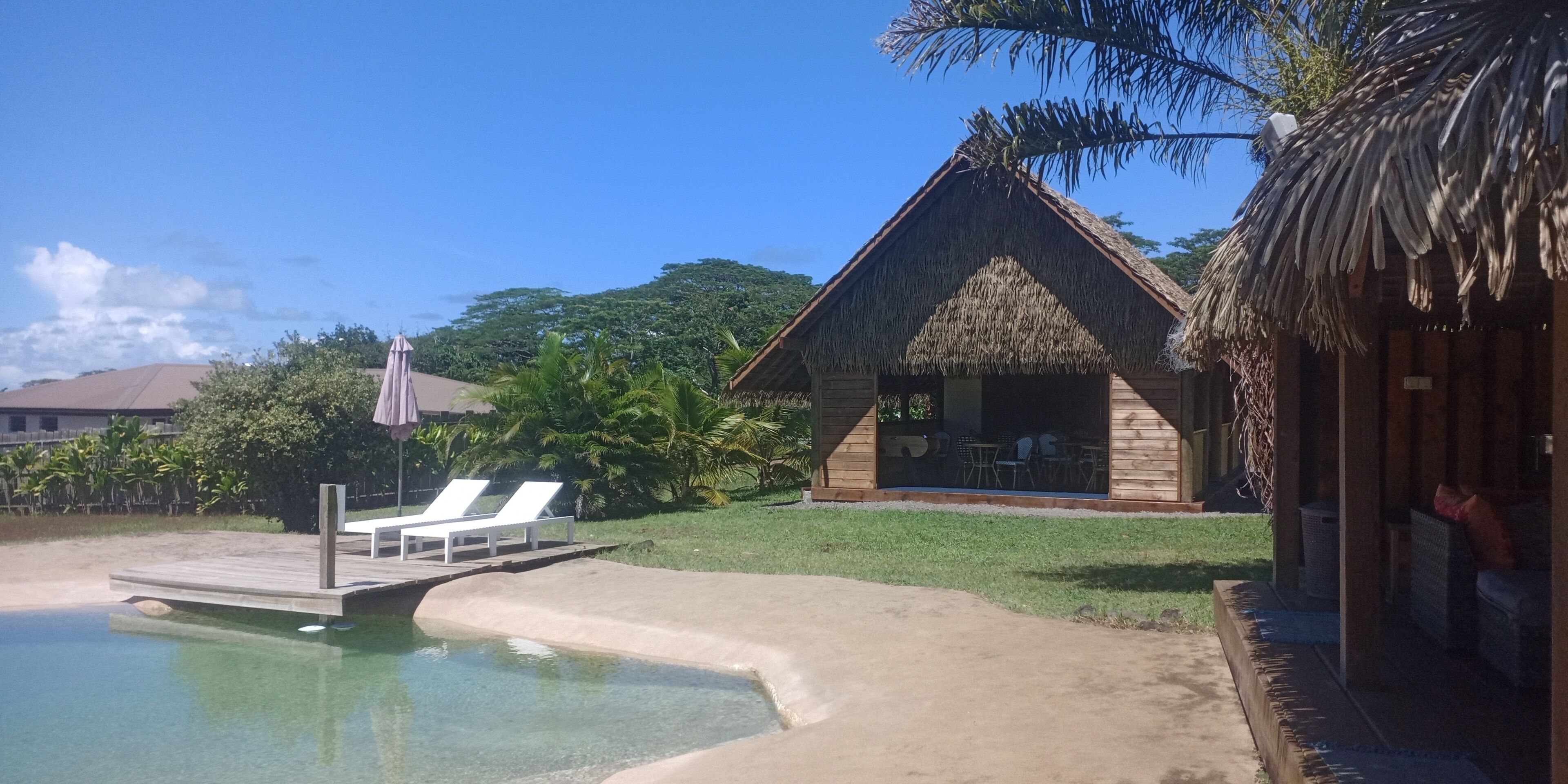 A resort with a pool, lounge chairs, and a thatched-roof building.