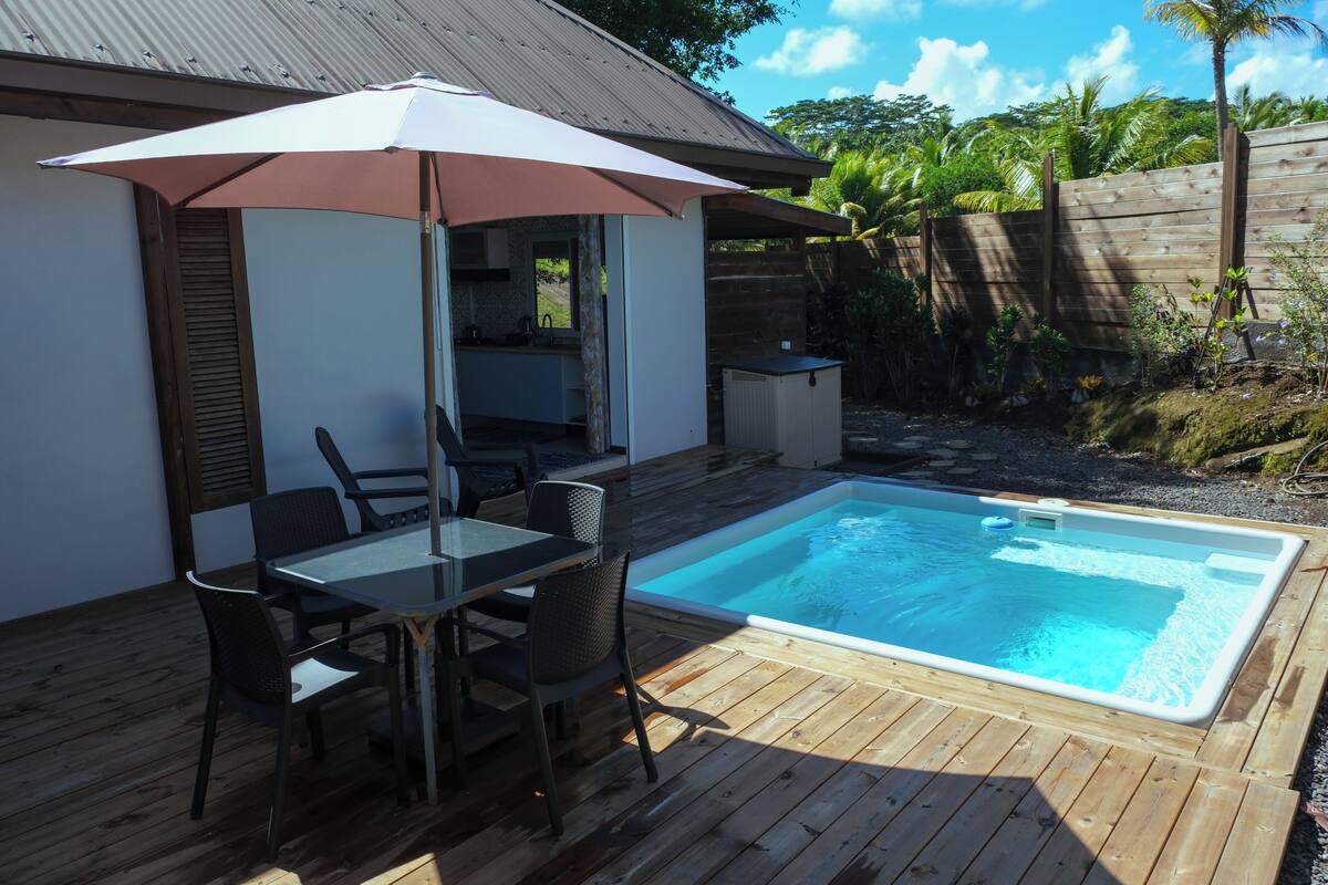 A poolside area with a table and chairs, a covered umbrella, and a wooden deck.